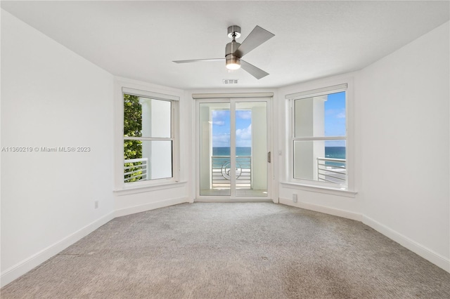 unfurnished room with light carpet, ceiling fan, and a water view