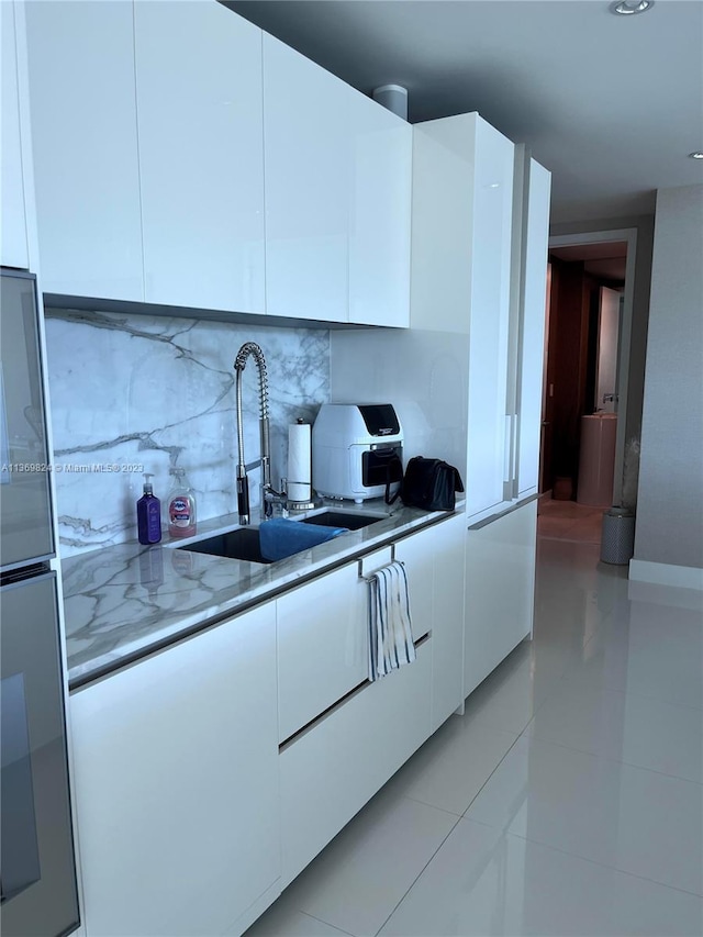 kitchen featuring light tile flooring, tasteful backsplash, white cabinetry, and sink