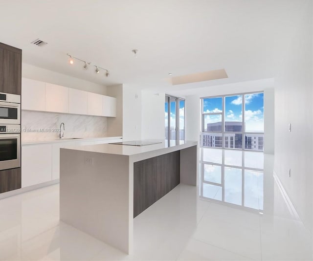 kitchen featuring stainless steel double oven, track lighting, light tile floors, white cabinets, and a center island