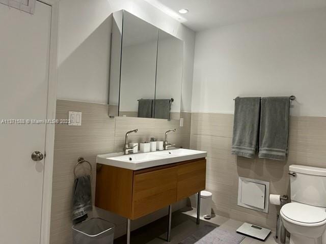 bathroom featuring tile walls, toilet, vanity, and tile flooring