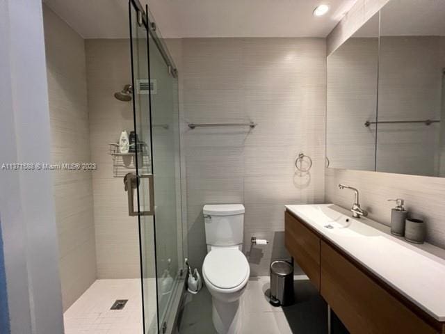 bathroom with tile walls, a shower with door, large vanity, and toilet