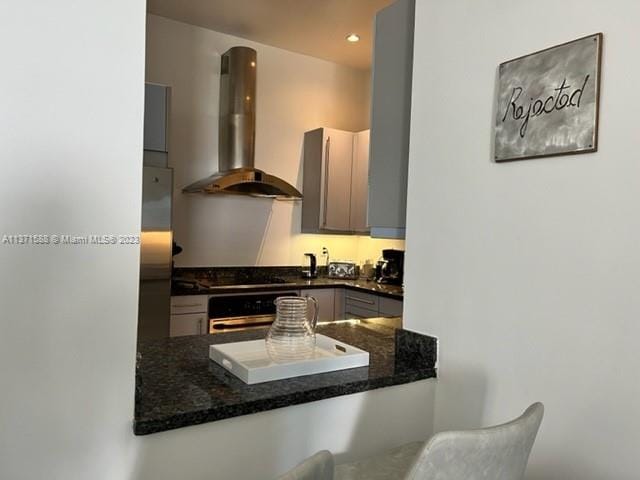 kitchen featuring black cooktop, dark stone counters, wall chimney range hood, stainless steel oven, and gray cabinetry