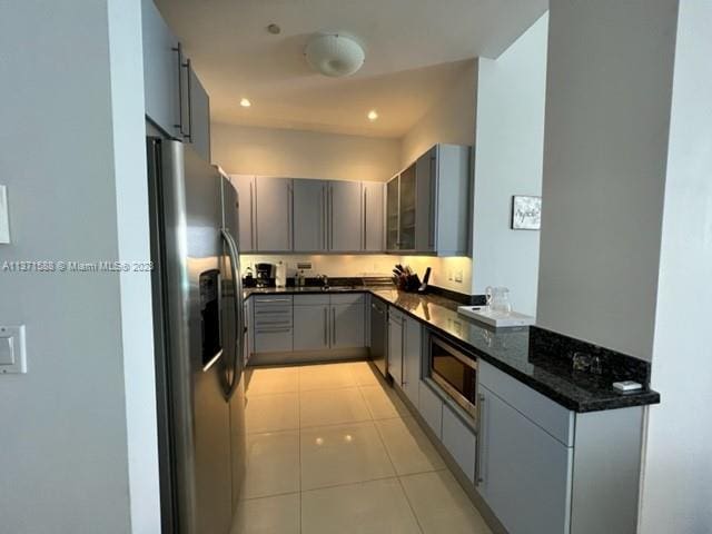 kitchen featuring light tile floors, gray cabinetry, dark stone countertops, and stainless steel appliances