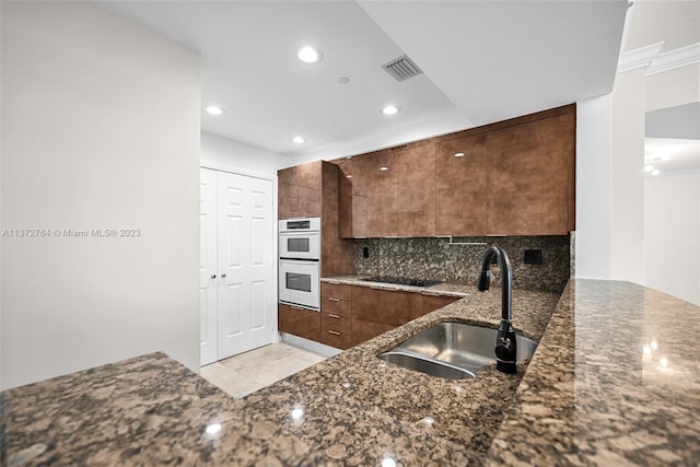 kitchen featuring white double oven, dark stone countertops, light tile floors, backsplash, and sink