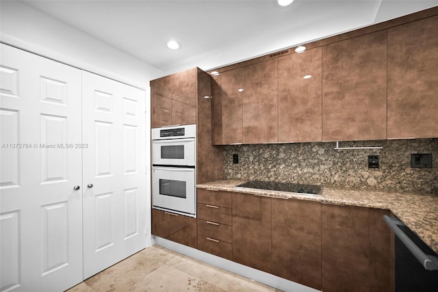 kitchen with dark brown cabinetry, black electric stovetop, light tile floors, dark stone countertops, and double oven