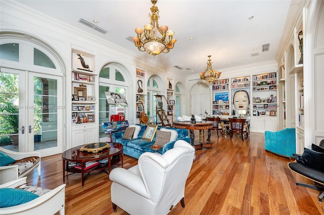 living room featuring built in features, light hardwood / wood-style floors, a notable chandelier, and french doors