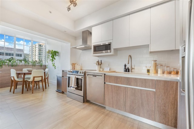 kitchen featuring appliances with stainless steel finishes, wall chimney range hood, light tile floors, sink, and white cabinets