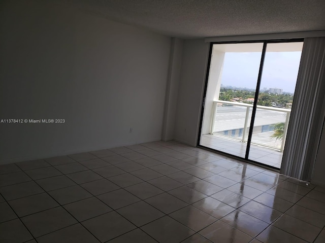 empty room featuring a textured ceiling, tile floors, and a wall of windows