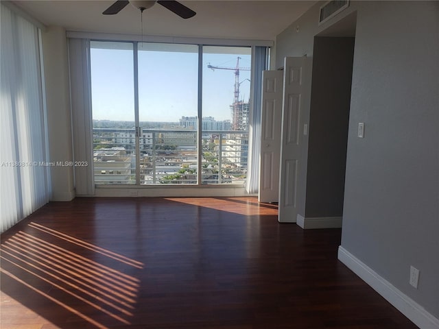 empty room featuring a wall of windows, ceiling fan, and dark wood-type flooring