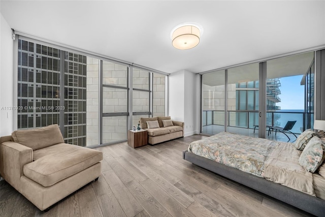 bedroom featuring a water view, expansive windows, access to outside, and light hardwood / wood-style flooring