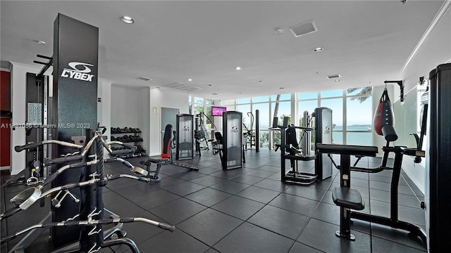 gym with a wall of windows, dark tile floors, ornamental molding, and a water view