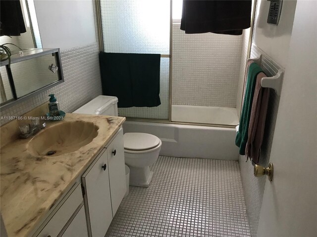 full bathroom featuring tile walls, toilet, tile flooring, combined bath / shower with glass door, and vanity