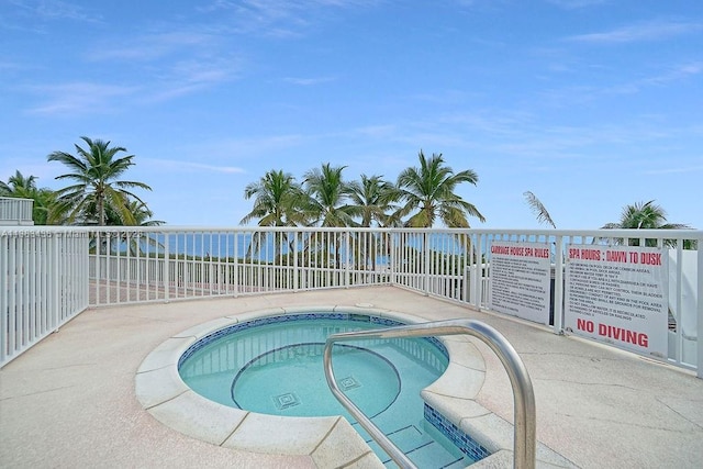 view of swimming pool featuring a water view, fence, and a hot tub