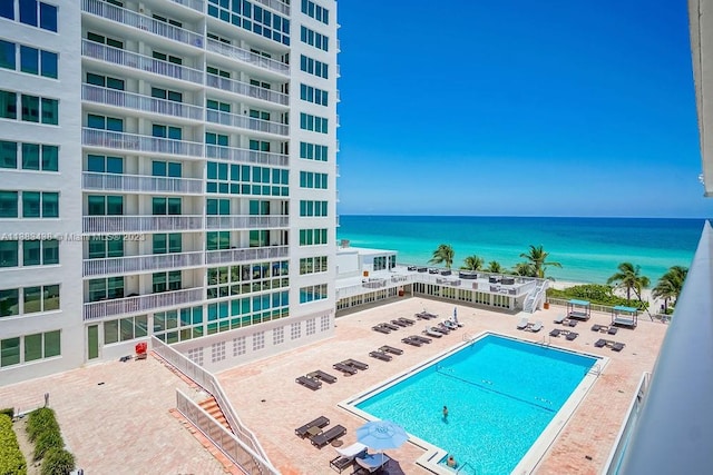 community pool with a patio area, a water view, and fence