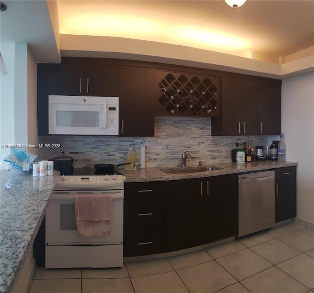 kitchen featuring white appliances, a sink, dark brown cabinetry, and light stone countertops