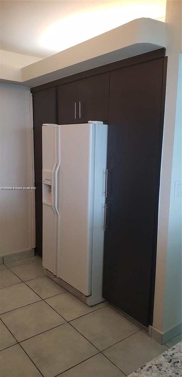 kitchen with light tile patterned floors, white refrigerator with ice dispenser, and dark brown cabinetry