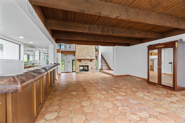 interior space with brick wall, a brick fireplace, light tile floors, beam ceiling, and wood ceiling