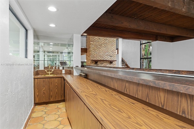 kitchen featuring light tile floors, a brick fireplace, wooden ceiling, beamed ceiling, and sink