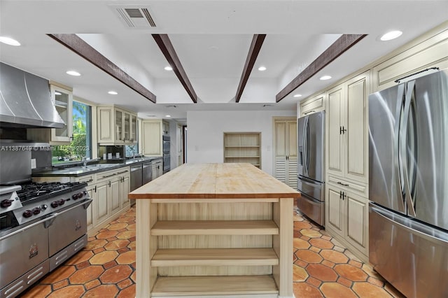 kitchen with wood counters, stainless steel appliances, light tile floors, a center island, and wall chimney exhaust hood