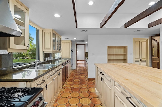 kitchen with butcher block counters, light tile floors, sink, and wall chimney range hood