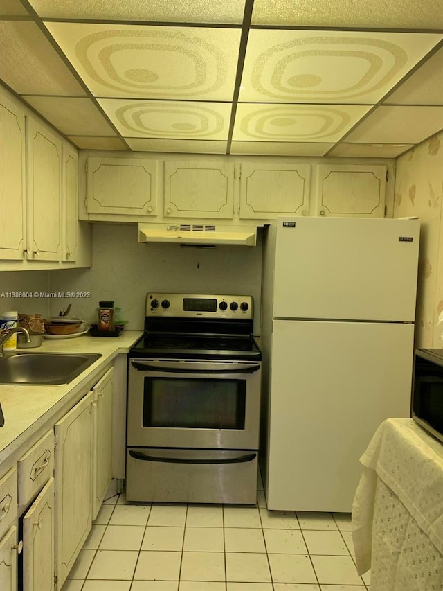 kitchen with appliances with stainless steel finishes, a drop ceiling, sink, and light tile flooring