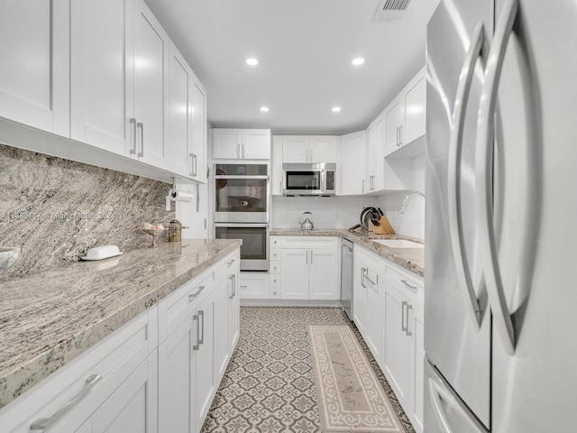 kitchen with white cabinetry, appliances with stainless steel finishes, light stone countertops, decorative backsplash, and sink