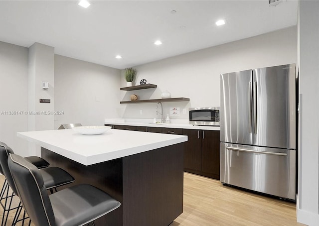 kitchen featuring appliances with stainless steel finishes, dark brown cabinetry, light hardwood / wood-style flooring, a kitchen breakfast bar, and a center island