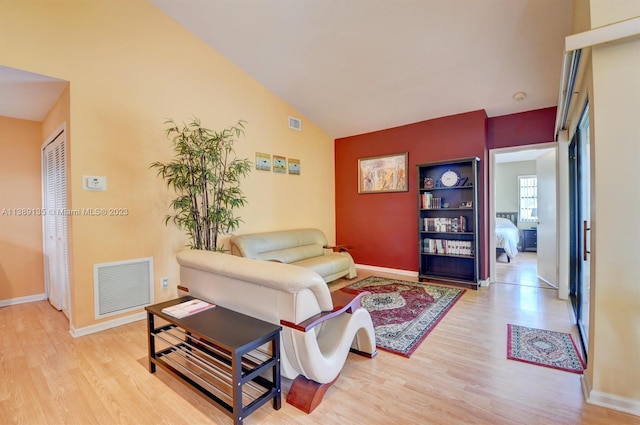 living room with lofted ceiling, built in shelves, and light wood-type flooring