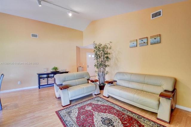 living room featuring high vaulted ceiling, rail lighting, and light hardwood / wood-style floors