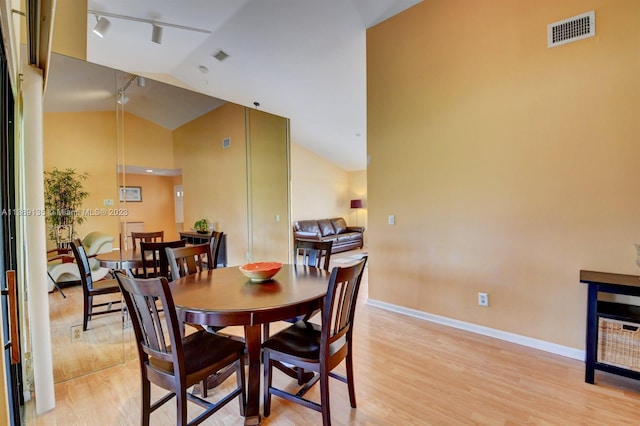 dining room featuring track lighting, high vaulted ceiling, and light hardwood / wood-style floors