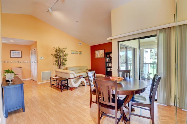 dining space with track lighting, lofted ceiling, and light wood-type flooring