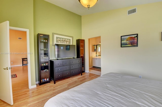 bedroom featuring light hardwood / wood-style floors, ensuite bathroom, and a high ceiling