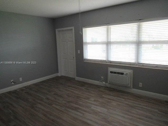 unfurnished room with dark wood-type flooring and an AC wall unit