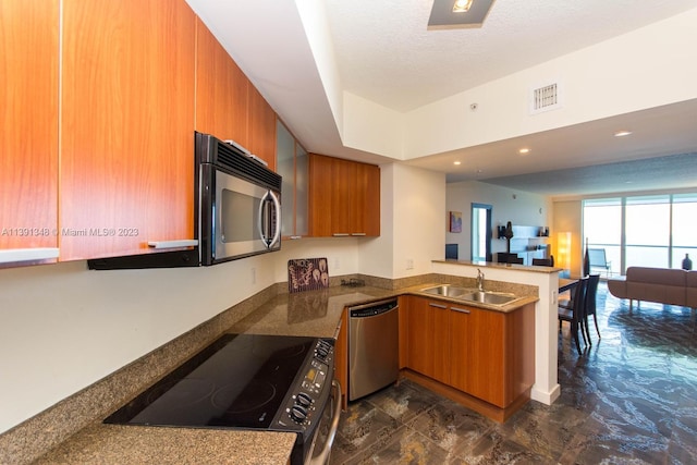 kitchen with appliances with stainless steel finishes, dark tile flooring, kitchen peninsula, and sink