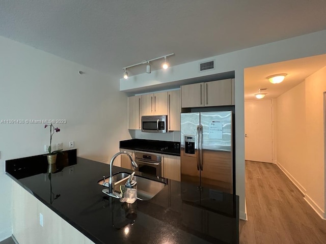 kitchen featuring appliances with stainless steel finishes, light brown cabinetry, rail lighting, and hardwood / wood-style flooring