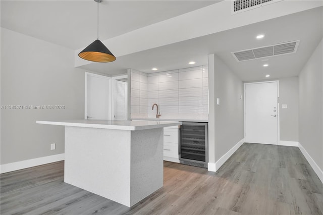 kitchen with beverage cooler, hanging light fixtures, a center island, white cabinets, and hardwood / wood-style flooring