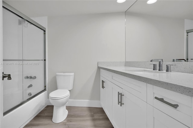 full bathroom featuring vanity with extensive cabinet space, enclosed tub / shower combo, toilet, and hardwood / wood-style flooring