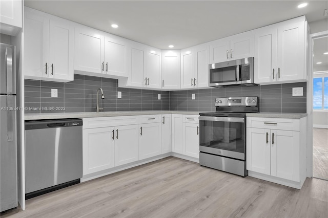 kitchen featuring white cabinets, tasteful backsplash, light wood-type flooring, and stainless steel appliances