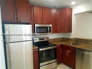 kitchen with sink, stainless steel appliances, and dark stone counters