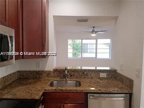 kitchen featuring stainless steel dishwasher, stone countertops, ceiling fan, and sink