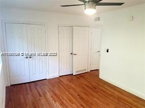 unfurnished bedroom with dark hardwood / wood-style floors, ceiling fan, and multiple closets