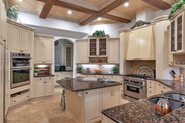 kitchen with coffered ceiling, backsplash, stainless steel appliances, dark stone countertops, and beam ceiling