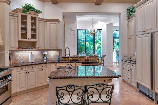 kitchen with a breakfast bar, a center island with sink, dark stone counters, a chandelier, and high end stove