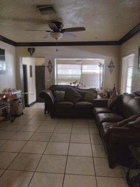 tiled living room with ornamental molding and ceiling fan