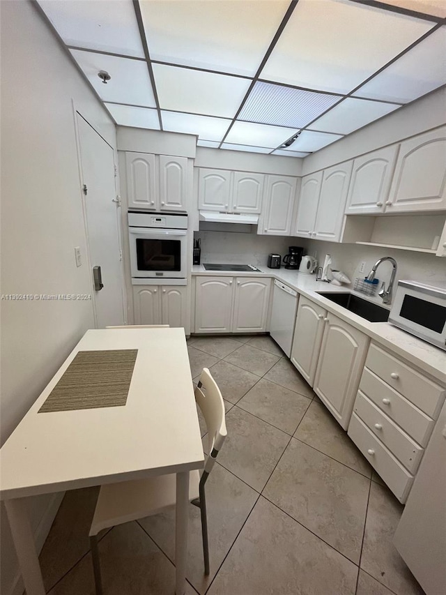 kitchen featuring a paneled ceiling, sink, white appliances, light tile flooring, and white cabinetry