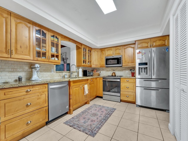 kitchen with backsplash, stainless steel appliances, light tile floors, and light stone countertops