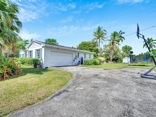 ranch-style home with a front lawn, a trampoline, a garage, and a storage shed