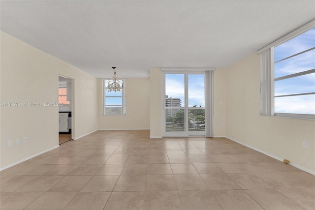 empty room with light tile patterned floors, a textured ceiling, baseboards, and an inviting chandelier