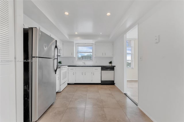 kitchen featuring dark countertops, a raised ceiling, white cabinetry, light tile patterned flooring, and white appliances