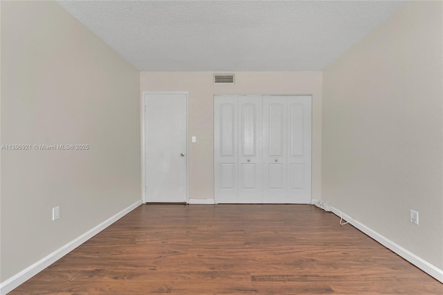 unfurnished bedroom featuring a textured ceiling, a closet, wood finished floors, and visible vents